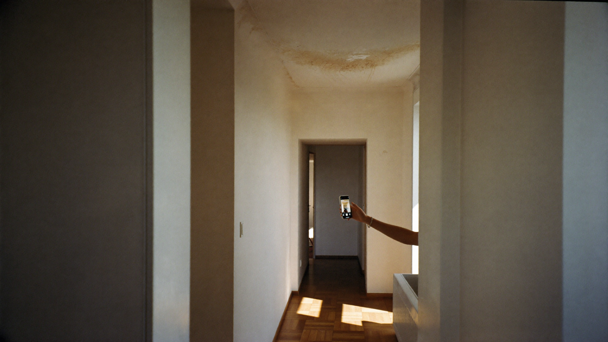 Founder-led home-watch property inspection in an Athens apartment — a hand photographs a small ceiling moisture stain during a scheduled Estia visit